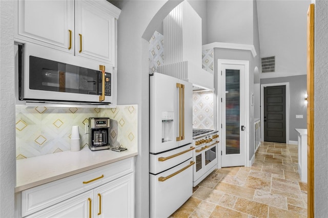 kitchen featuring a towering ceiling, white appliances, white cabinets, and tasteful backsplash