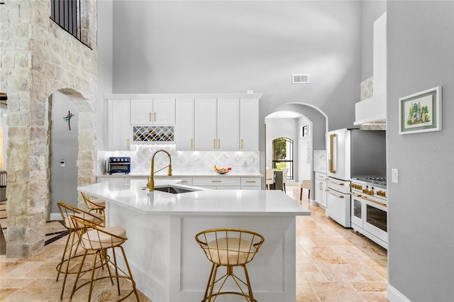 kitchen featuring a high ceiling, high quality appliances, sink, a breakfast bar, and white cabinets