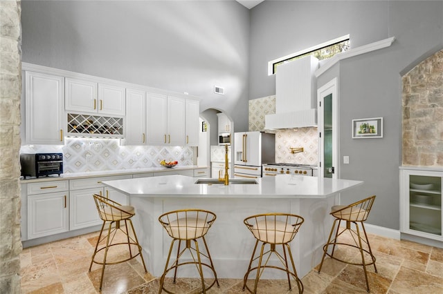 kitchen featuring a kitchen island with sink, white cabinets, backsplash, and a high ceiling