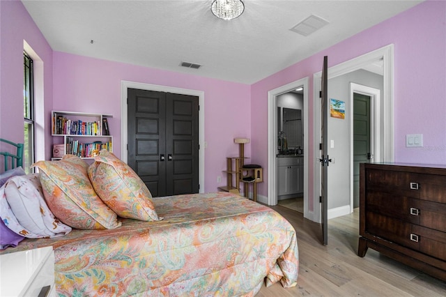 bedroom featuring a textured ceiling, connected bathroom, a closet, and light wood-type flooring