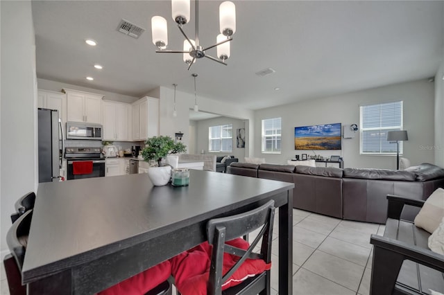 kitchen featuring pendant lighting, a chandelier, light tile patterned floors, stainless steel appliances, and white cabinets