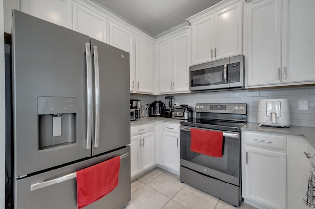 kitchen featuring light tile patterned floors, appliances with stainless steel finishes, white cabinets, and decorative backsplash