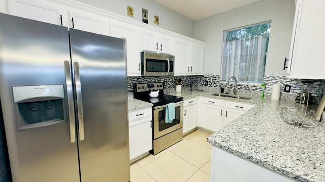 kitchen featuring light tile patterned floors, appliances with stainless steel finishes, a sink, light stone countertops, and backsplash