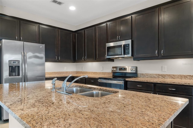 kitchen featuring a kitchen island with sink, light stone counters, stainless steel appliances, and sink