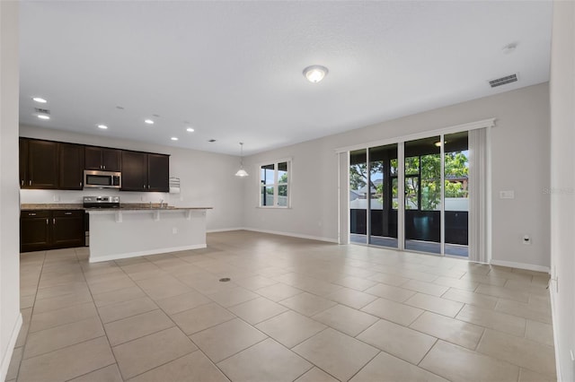 kitchen featuring a kitchen bar, stainless steel appliances, a center island with sink, light tile patterned flooring, and dark brown cabinetry