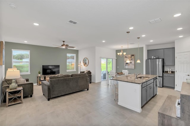 kitchen featuring gray cabinetry, sink, light stone countertops, an island with sink, and appliances with stainless steel finishes