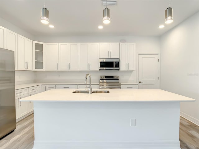 kitchen with a center island with sink, stainless steel appliances, sink, white cabinets, and light hardwood / wood-style flooring