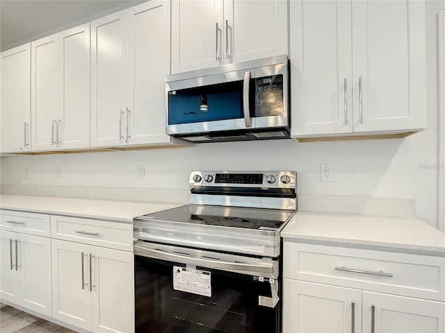 kitchen with stainless steel appliances, light hardwood / wood-style floors, white cabinetry, and light stone counters