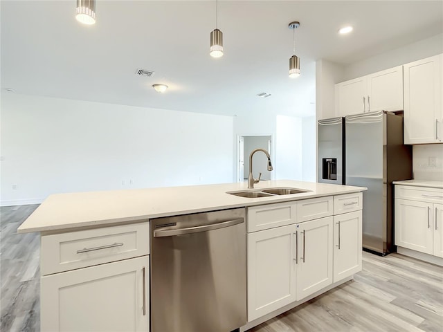 kitchen featuring stainless steel appliances, white cabinets, hanging light fixtures, sink, and light wood-type flooring