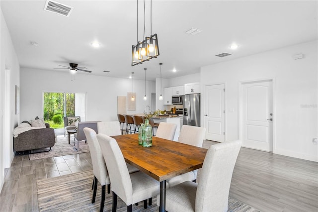 dining room featuring ceiling fan with notable chandelier, sink, and light hardwood / wood-style floors