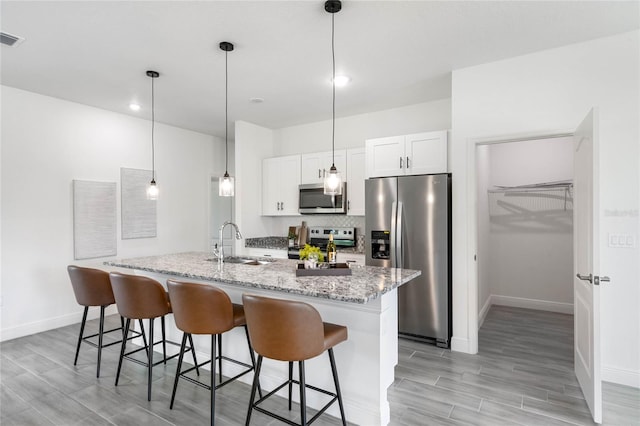 kitchen with appliances with stainless steel finishes, white cabinetry, sink, an island with sink, and pendant lighting