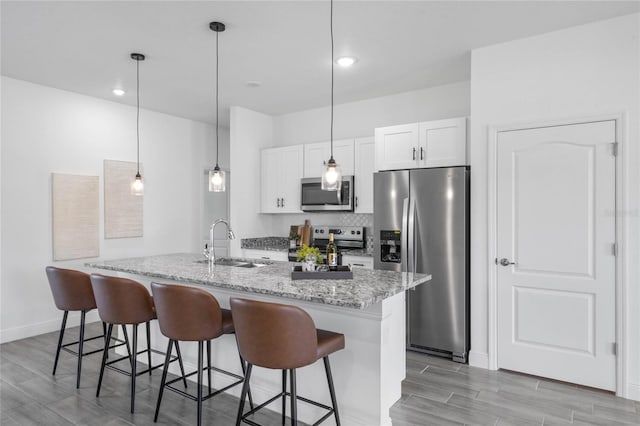 kitchen with white cabinetry, decorative light fixtures, an island with sink, sink, and appliances with stainless steel finishes