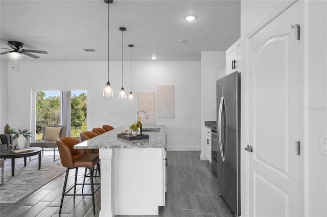 kitchen with a kitchen island with sink, stainless steel fridge, decorative light fixtures, a kitchen breakfast bar, and white cabinets