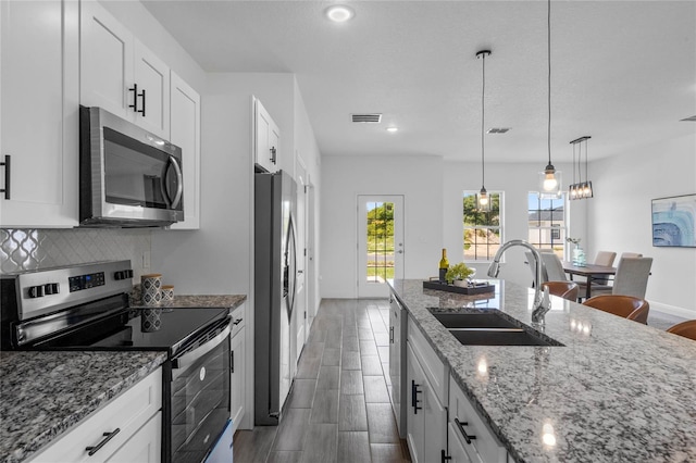 kitchen with light stone countertops, pendant lighting, appliances with stainless steel finishes, sink, and white cabinets