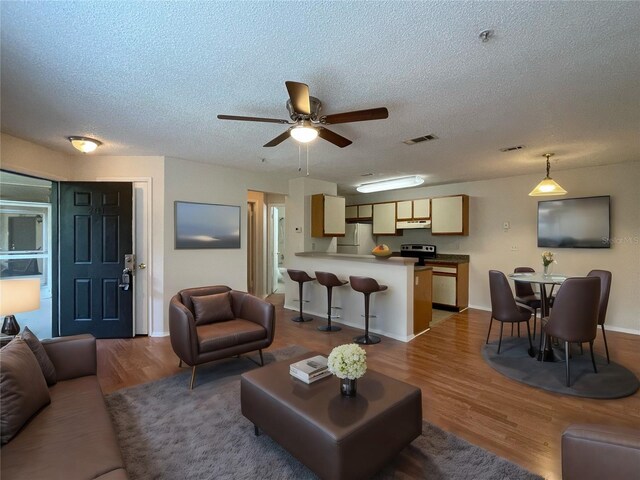 living room with ceiling fan, hardwood / wood-style flooring, and a textured ceiling