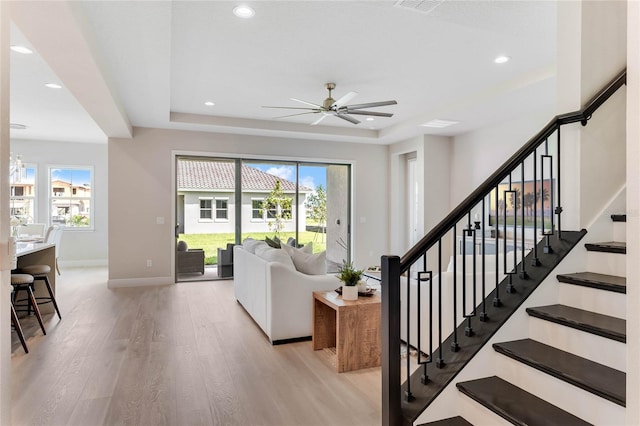 living room featuring ceiling fan, a tray ceiling, and light hardwood / wood-style floors