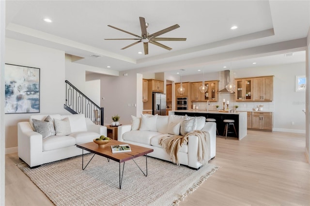 living room featuring a tray ceiling, light hardwood / wood-style flooring, sink, and ceiling fan