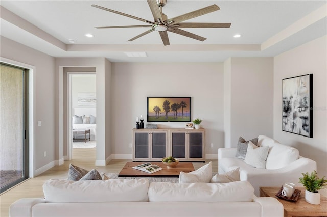 living room featuring ceiling fan, a raised ceiling, and light hardwood / wood-style floors