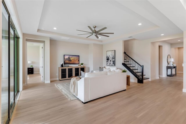 living room featuring light wood-type flooring, ceiling fan, a raised ceiling, and a healthy amount of sunlight