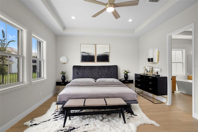 bedroom with a tray ceiling, multiple windows, light hardwood / wood-style flooring, and ceiling fan