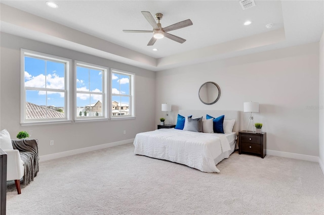 bedroom with a raised ceiling, light colored carpet, and ceiling fan