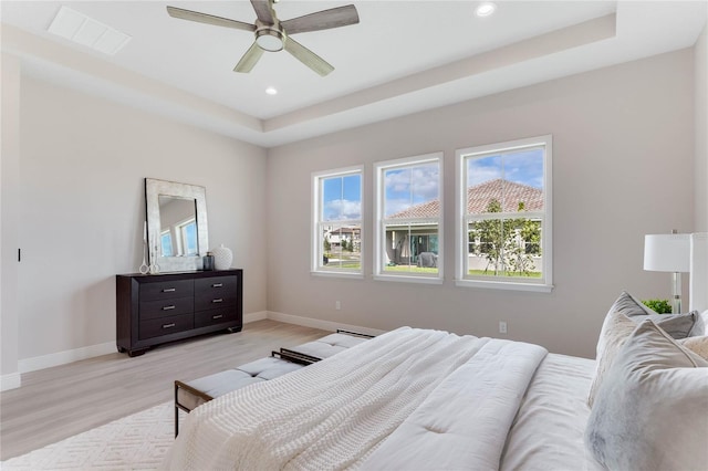 bedroom with ceiling fan, light wood-type flooring, and a tray ceiling