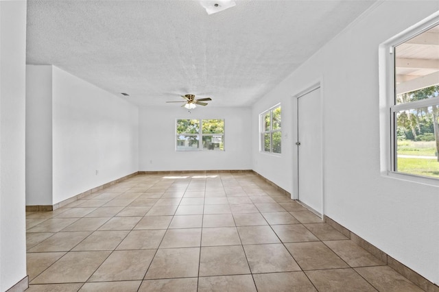 unfurnished room with ceiling fan, a textured ceiling, light tile patterned flooring, and baseboards