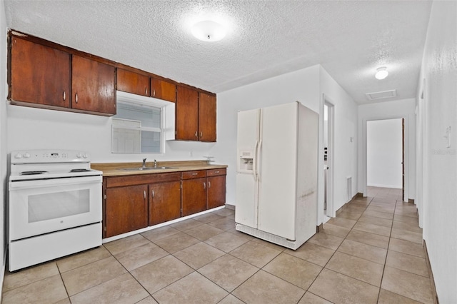 kitchen with light tile patterned floors, white appliances, a sink, light countertops, and brown cabinets