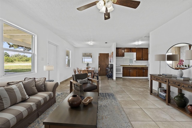 living area with ceiling fan, a textured ceiling, and light tile patterned floors