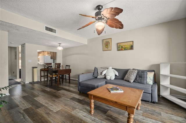 living room with dark wood-type flooring, ceiling fan, and a textured ceiling