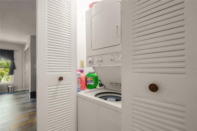 laundry area with a textured ceiling, stacked washer and clothes dryer, and hardwood / wood-style floors