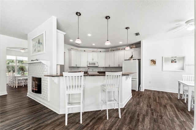 kitchen with a brick fireplace, white appliances, dark hardwood / wood-style floors, ceiling fan, and a breakfast bar