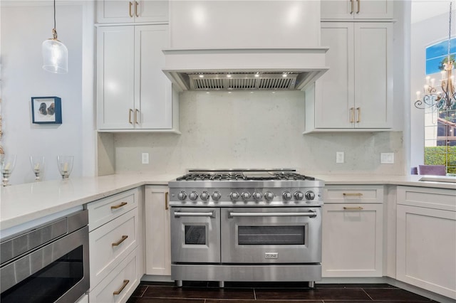 kitchen featuring appliances with stainless steel finishes, hanging light fixtures, white cabinetry, dark wood-type flooring, and wall chimney range hood