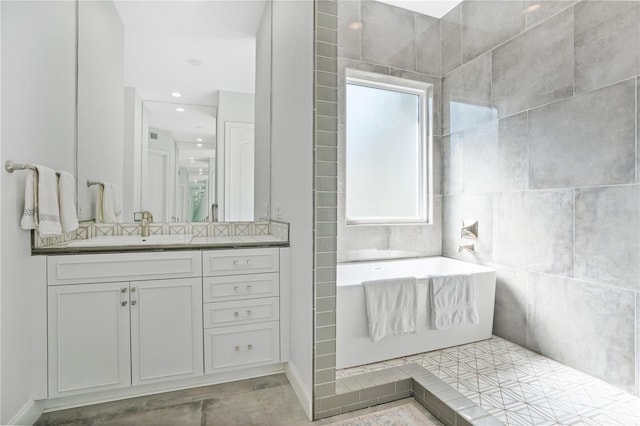 bathroom with tile walls, vanity, tile patterned flooring, and a bathtub