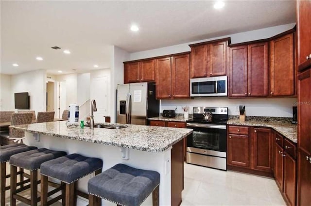 kitchen featuring a kitchen breakfast bar, light stone countertops, appliances with stainless steel finishes, a kitchen island with sink, and sink