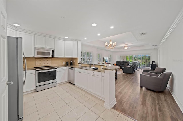 kitchen featuring white cabinets, light hardwood / wood-style flooring, appliances with stainless steel finishes, a raised ceiling, and kitchen peninsula