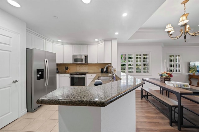 kitchen with a notable chandelier, decorative light fixtures, kitchen peninsula, sink, and appliances with stainless steel finishes