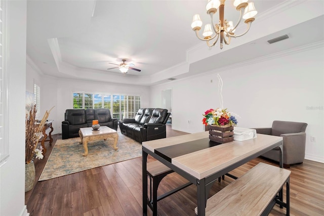 dining room with crown molding, a raised ceiling, ceiling fan with notable chandelier, and dark wood-type flooring