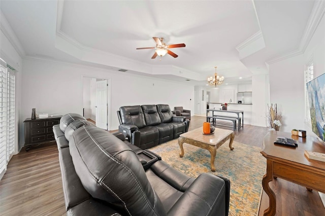 living room with ceiling fan with notable chandelier, crown molding, hardwood / wood-style flooring, and a tray ceiling