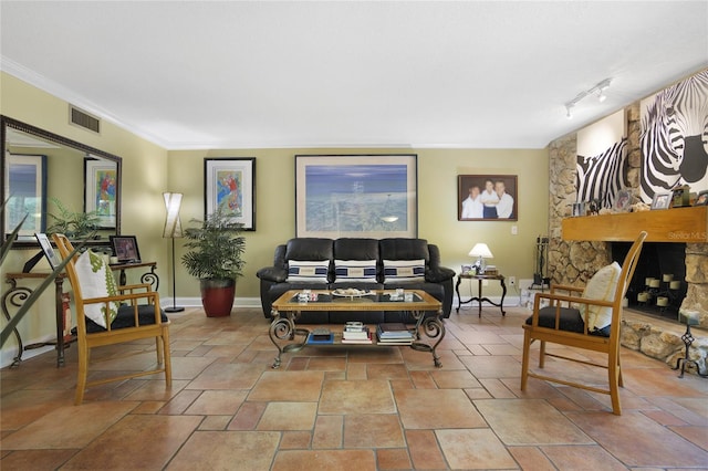 living room with crown molding, a stone fireplace, and track lighting