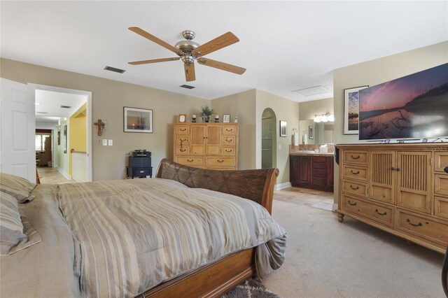 bedroom with light colored carpet, ensuite bath, and ceiling fan