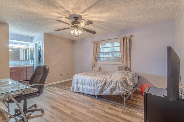 bedroom featuring light wood-type flooring, ensuite bath, ceiling fan, and a textured ceiling