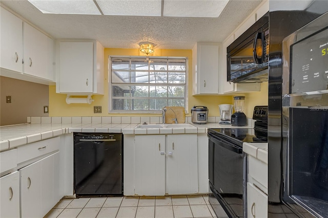kitchen featuring white cabinets, light tile patterned floors, black appliances, tile counters, and sink