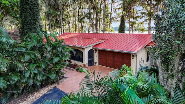 view of front facade with driveway, a garage, metal roof, a standing seam roof, and stucco siding