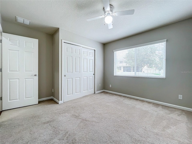 unfurnished bedroom with a textured ceiling, light colored carpet, ceiling fan, and a closet