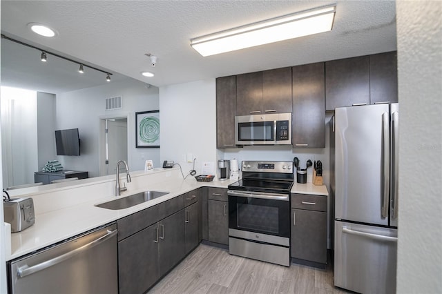 kitchen featuring a textured ceiling, kitchen peninsula, sink, appliances with stainless steel finishes, and light hardwood / wood-style floors