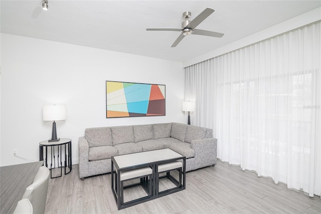 living room with light wood-type flooring, ceiling fan, and a textured ceiling