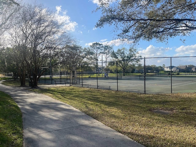 view of tennis court with a yard and fence