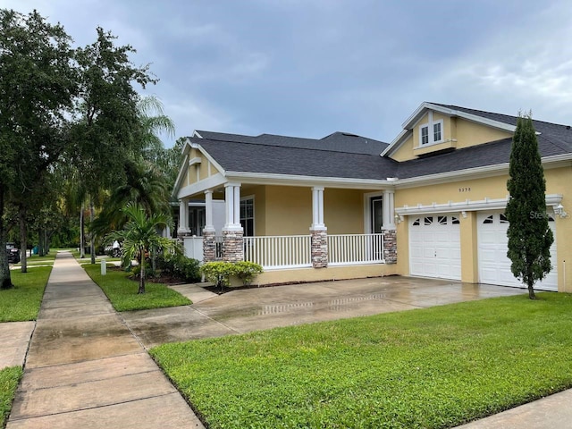 view of front of property featuring a porch, a front yard, stucco siding, a garage, and driveway