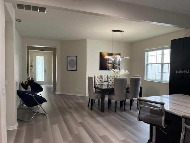 dining area with wood finished floors, visible vents, a chandelier, and baseboards